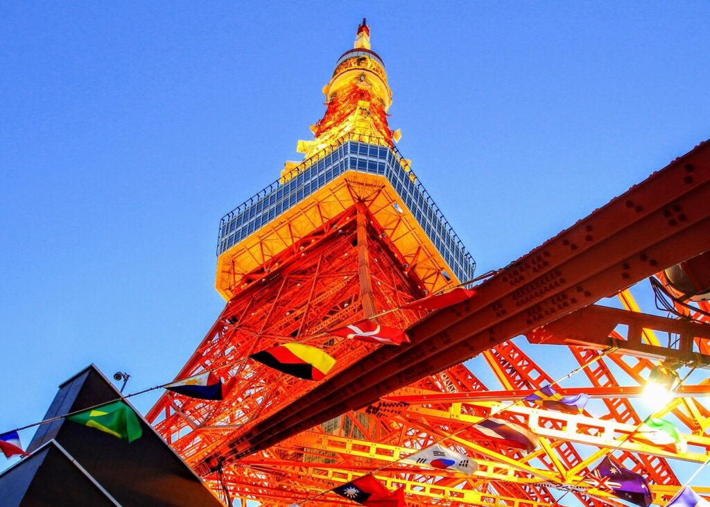 Tokyo Tower glows orange against a clear blue sky in Japan, with colorful pennants fluttering in the foreground.