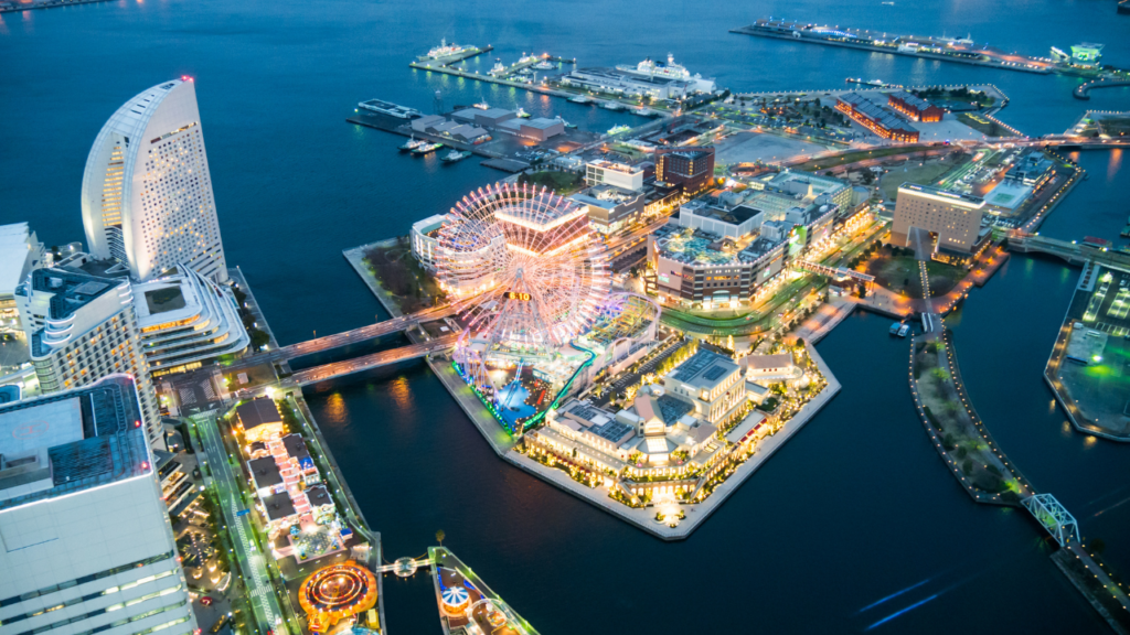 Aerial night view of a Yokohama waterfront with a giant illuminated Ferris wheel and glowing modern towers.