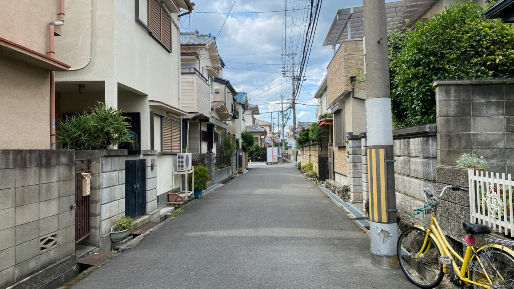 Quiet Tokyo street in Japan: narrow walking road flanked by walls, potted plants, and a yellow bicycle by a striped pole.
