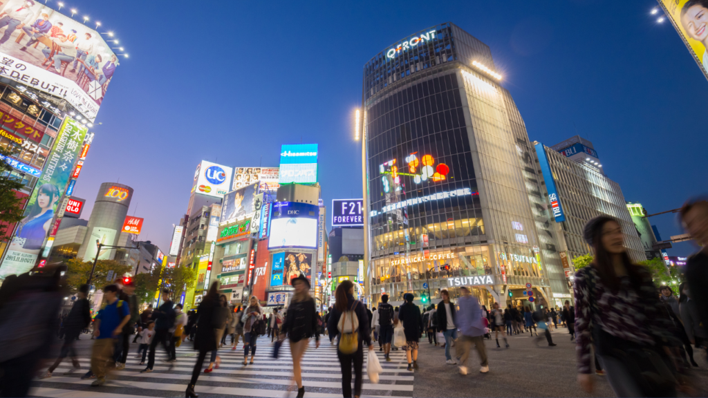 Busy Shibuya Crossing in Tokyo, Japan at twilight, crowds walking under neon billboards past gleaming glass towers, travel.