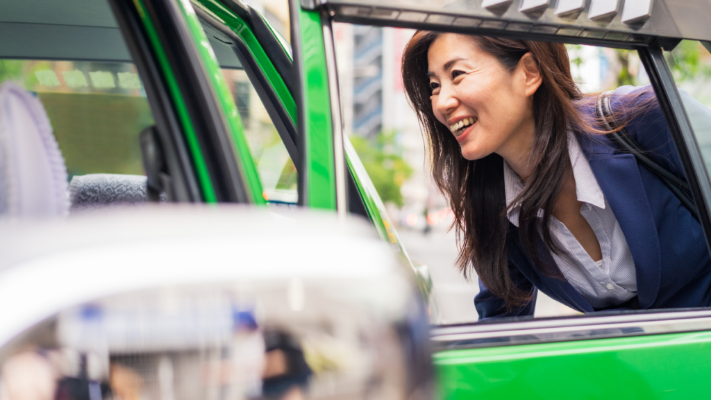 Smiling woman in a blue blazer leans out of a bright green taxi window on a Tokyo street, travel in Japan.