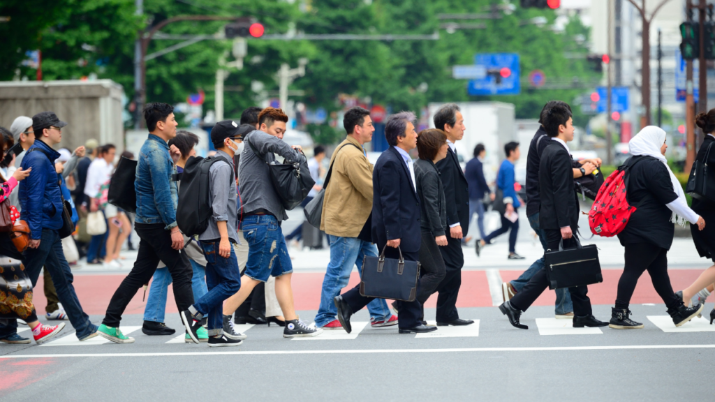 Busy Tokyo crosswalk crowded with diverse pedestrians, business professionals, students, and travelers with bags.