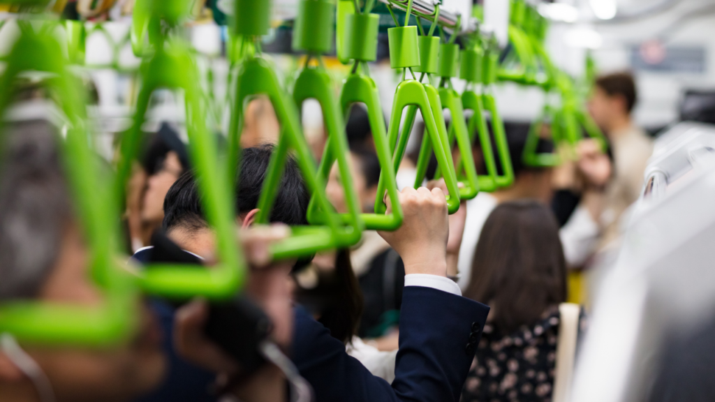Crowded Tokyo subway car during travel with bright green handrails and hanging straps, passengers standing and gripping.