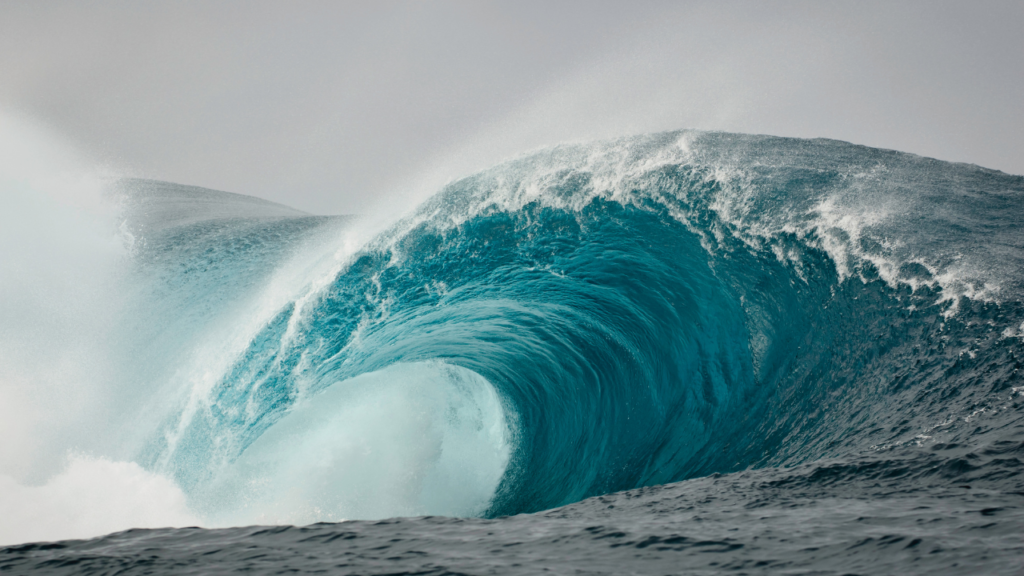 Massive turquoise wave curls into a perfect barrel, spray and mist flinging as the seascape roars.