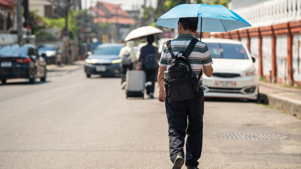 Traveling with blue umbrella, walking down Tokyo, Japan street, striped shirt, black backpack, luggage by curb, cars ahead.